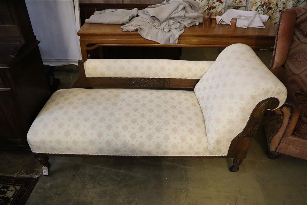 A late 19th century chaise longue with carved oak frame on turned legs and castors